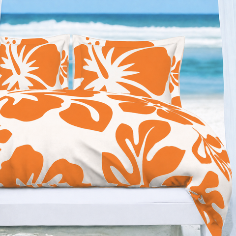A bed dressed in a white duvet cover and matching pillowcases with a bold orange tropical floral pattern, set against a beach background with ocean waves and a white cabana.